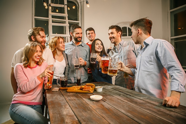 Grupo de amigos, desfrutando de bebidas à noite com cerveja na mesa de madeira