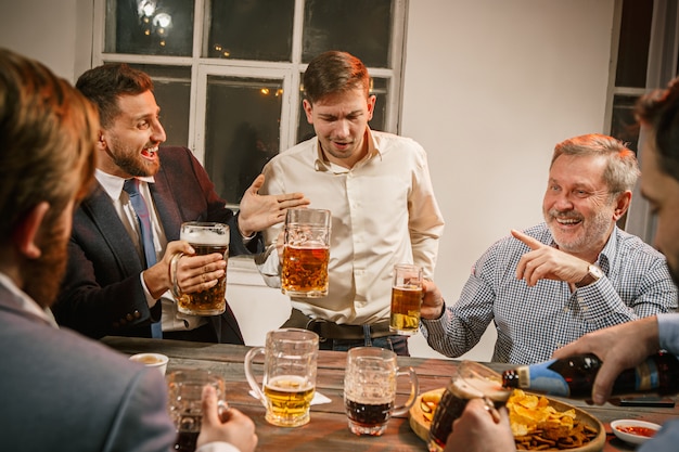Grupo de amigos, desfrutando de bebidas à noite com cerveja na mesa de madeira