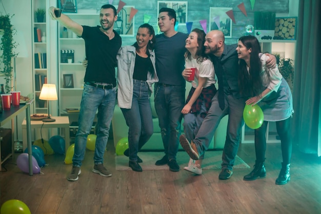 Grupo de amigos fazendo uma festa em um apartamento e fazendo uma selfie.