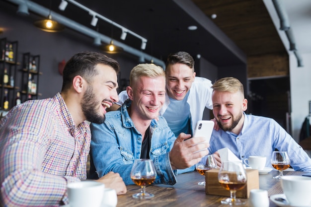 Grupo de amigos felizes olhando para smartphone sentado no restaurante