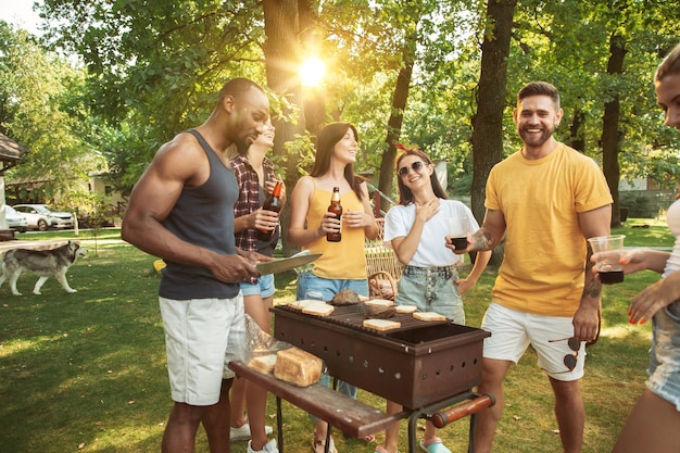 Grupo de amigos felizes, tendo uma festa de cerveja e churrasco em dia de sol. Descansando juntos ao ar livre em uma clareira na floresta ou quintal
