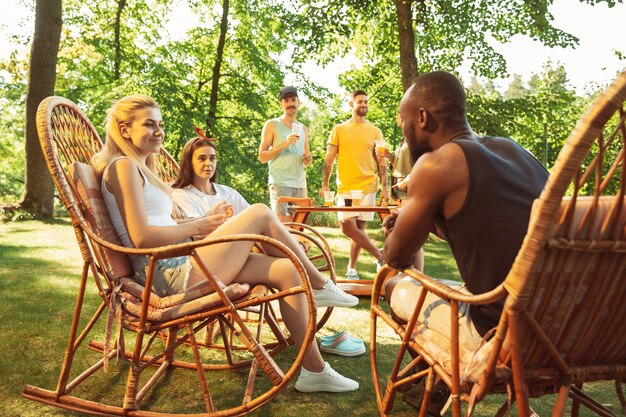 Grupo de amigos felizes, tendo uma festa de cerveja e churrasco em dia de sol. Descansando juntos ao ar livre em uma clareira na floresta ou quintal