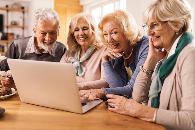 Grupo de amigos maduros felizes se divertindo enquanto navega na net em um computador em casa