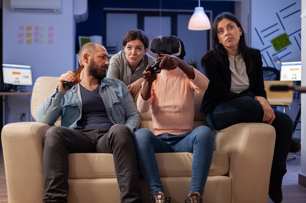 Grupo de amigos multiétnicos usando óculos VR para se divertir depois do trabalho no escritório