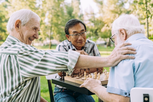 Grupo de amigos sênior jogando xadrez no parque. conceitos de estilo de vida sobre antiguidade e terceira idade