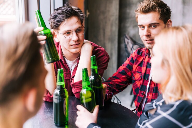 Foto grátis grupo de amigos sentados juntos segurando garrafas de cerveja verde