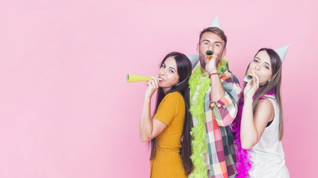 Grupo de amigos soprando corneta de festa em fundo rosa