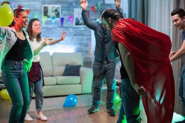 Grupo de amigos torcendo por homens com capa de super-herói na festa.