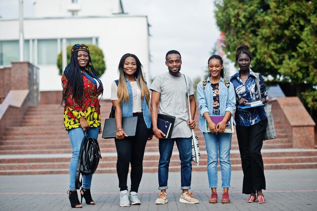 Grupo de cinco estudantes universitários africanos passando tempo juntos no campus no pátio da universidade Amigos negros afro estudando o tema da educação