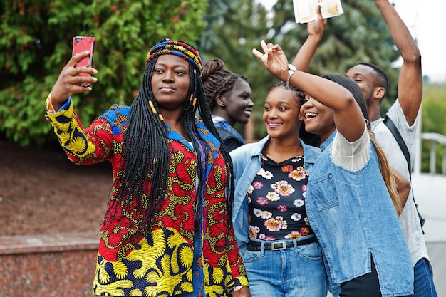 Foto grátis grupo de cinco estudantes universitários africanos passando tempo juntos no campus no pátio da universidade amigos negros afro fazendo selfie no telefone tema educacional