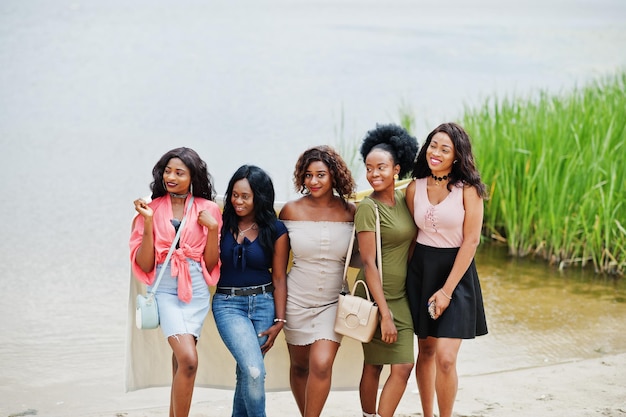 Grupo de cinco garotas afro-americanas em pé na areia contra o lago