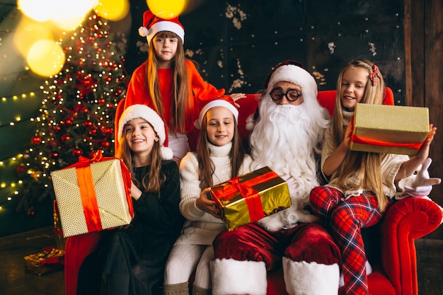 Grupo de crianças sentadas com o Papai Noel e presentes na véspera de Natal