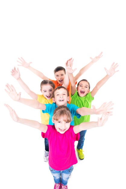 Grupo de crianças sorridentes com as mãos levantadas em camisetas coloridas, juntos. Vista do topo. Isolado no branco.