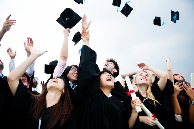 Grupo de diversos graduados jogando bonés no céu