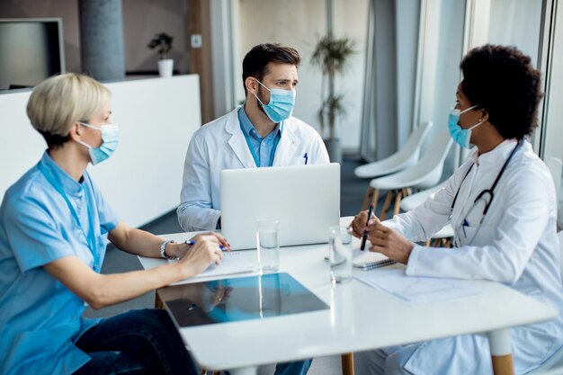 Grupo de especialistas em saúde com máscaras faciais conversando durante uma reunião na clínica médica