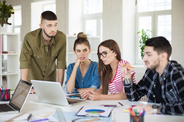 Grupo de homens e mulheres pensativos com laptop passando tempo no trabalho Jovens criativos pensando em um novo projeto juntos no escritório moderno