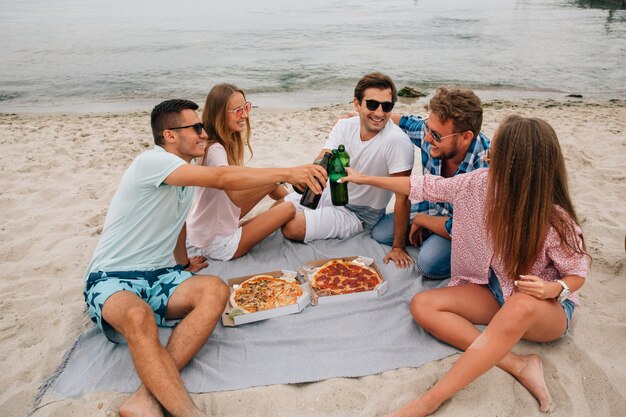 Grupo de jovens amigos atraentes fazendo um brinde, bebendo cerveja com pizza