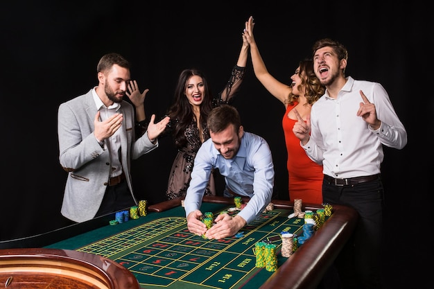 Grupo de jovens atrás da mesa de roleta em fundo preto. Jogador Vencedor. Emoções brilhantes