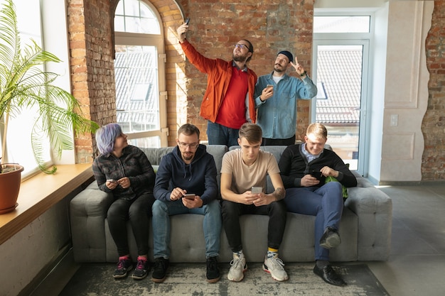 Grupo de jovens caucasianos felizes, sentados juntos em um sofá.