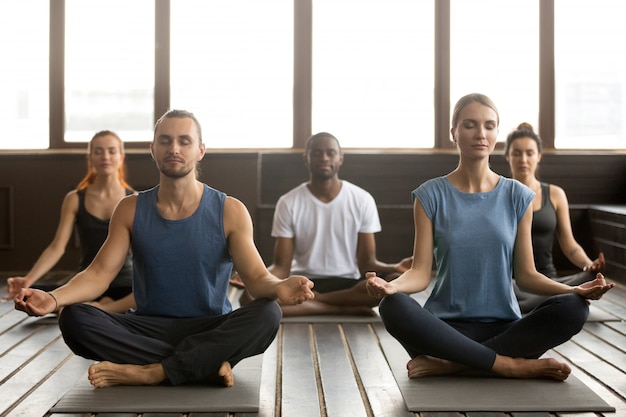 Grupo de jovens desportivos sentado no exercício de Sukhasana