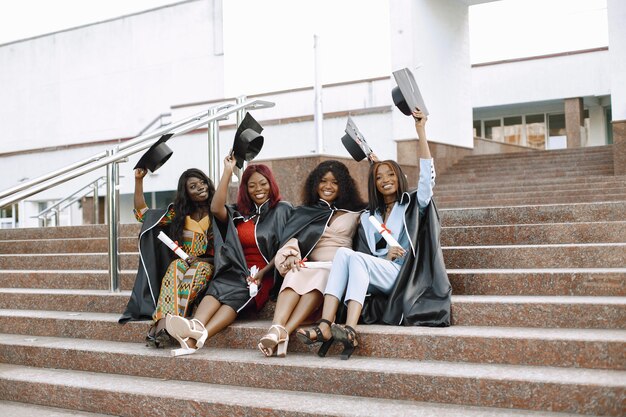 Grupo de jovens estudantes afro-americanas vestidas com vestido preto de formatura. Campus como pano de fundo