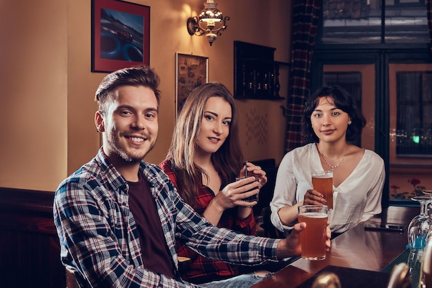 Foto grátis grupo de jovens sorridentes multirraciais descansando no pub. amigos sentados no balcão de madeira e desfrutando de bebidas.