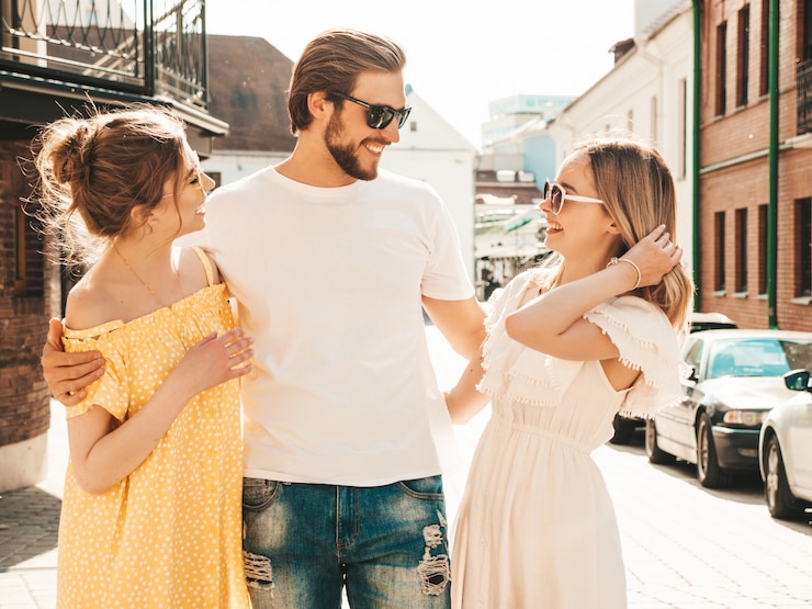 Foto grátis grupo de jovens três amigos elegantes posando na rua. homem moda e duas miúdas giras vestidas com roupas de verão casual. sorrindo modelos se divertindo em óculos de sol. mulheres alegres e cara enlouquecendo