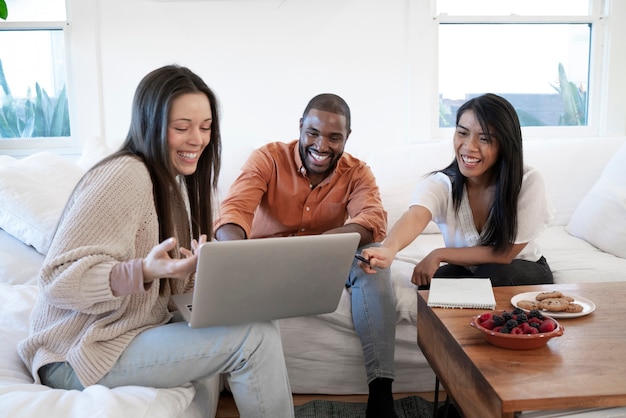 Grupo de jovens usando laptop juntos em casa no sofá e comendo lanches