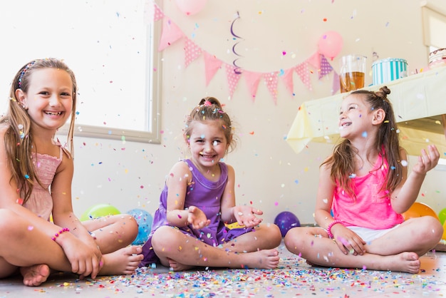 Grupo de meninas felizes brincando com confete durante a festa de aniversário