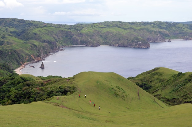 Grupo de pessoas caminhando nas montanhas ao redor de um mar cercado por vegetação sob um céu azul