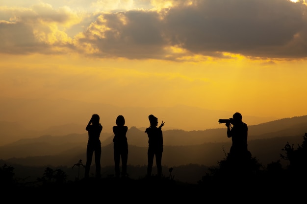 Grupo de pessoas felizes fotografando na montanha ao pôr do sol