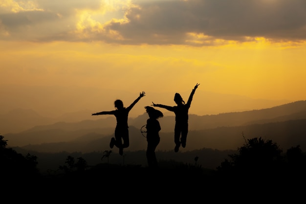 Grupo de pessoas felizes pulando na montanha ao pôr do sol