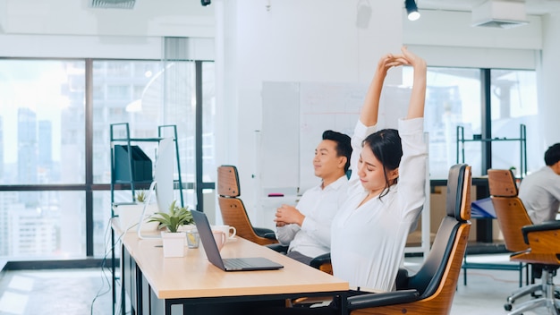 Grupo de processo colaborativo de empresários multiculturais em roupas casuais inteligentes se comunicando e usando a tecnologia enquanto trabalham juntos no escritório criativo. A equipe de jovens profissionais da Ásia trabalha.