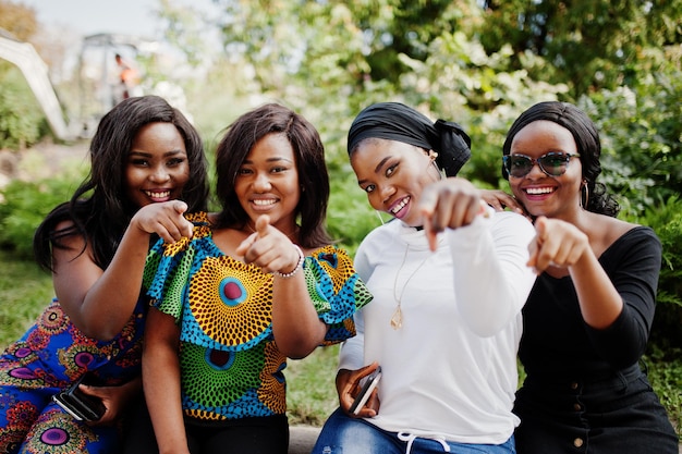 Grupo de quatro garotas afro-americanas sentadas ao ar livre e mostrando os dedos