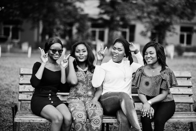 Grupo de quatro garotas afro-americanas sentadas no banco ao ar livre e colocar as mãos no ar