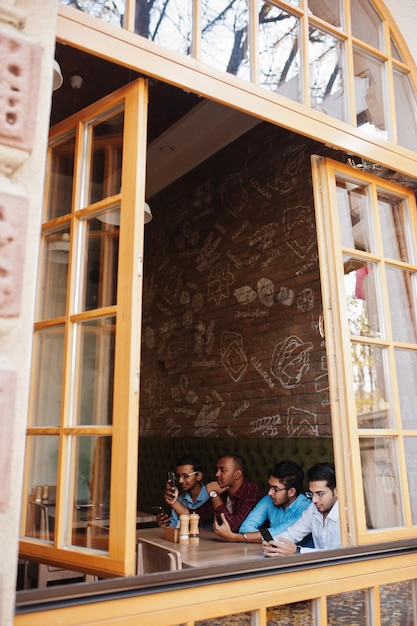 Grupo de quatro homens do sul da Ásia posaram em reunião de negócios no café índios trabalham juntos usando vários gadgets conversando