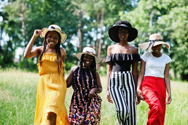 Grupo de quatro lindas mulheres afro-americanas usam chapéu de verão passando tempo na grama verde no parque