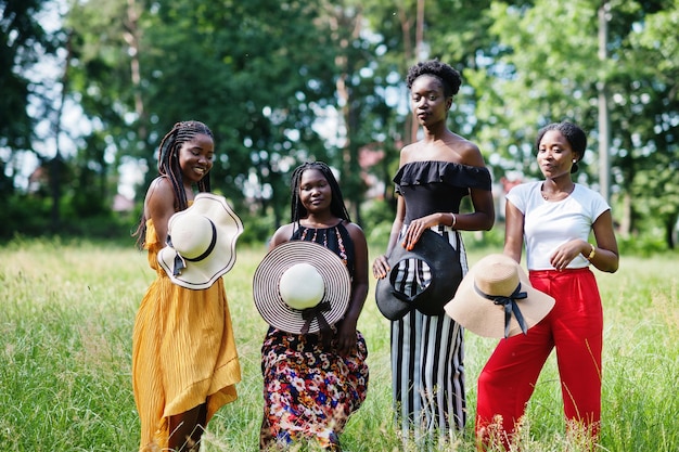 Grupo de quatro lindas mulheres afro-americanas usam chapéu de verão passando tempo na grama verde no parque
