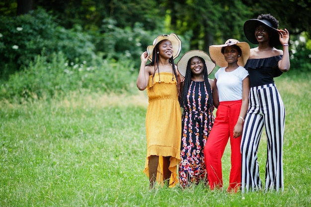 Grupo de quatro lindas mulheres afro-americanas usam chapéu de verão passando tempo na grama verde no parque