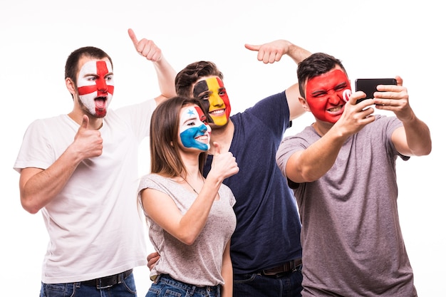 Grupo de torcedores apóia suas seleções com rostos pintados. inglaterra, bélgica, tunísia, panamá fãs tiram selfie no telefone isolado no fundo branco