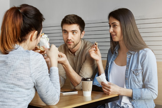 Grupo de três estudantes bonitos sentado no refeitório da universidade, almoçando, falando sobre os exames de ontem. Vida universitária.