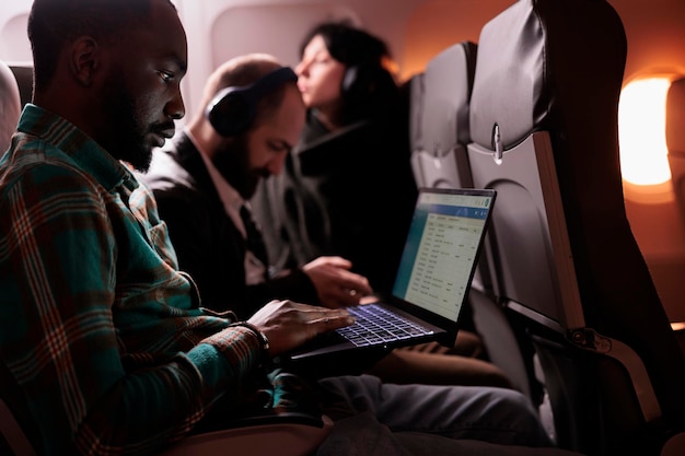 Grupo diversificado de passageiros voando em classe comercial juntos para chegar ao destino, homem usando computador portátil durante o voo internacional. Turistas viajando para o exterior de avião.