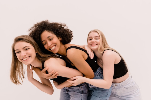 Grupo interracial de três belas jovens amigas em roupas casuais sorrindo e se divertindo em fundo branco