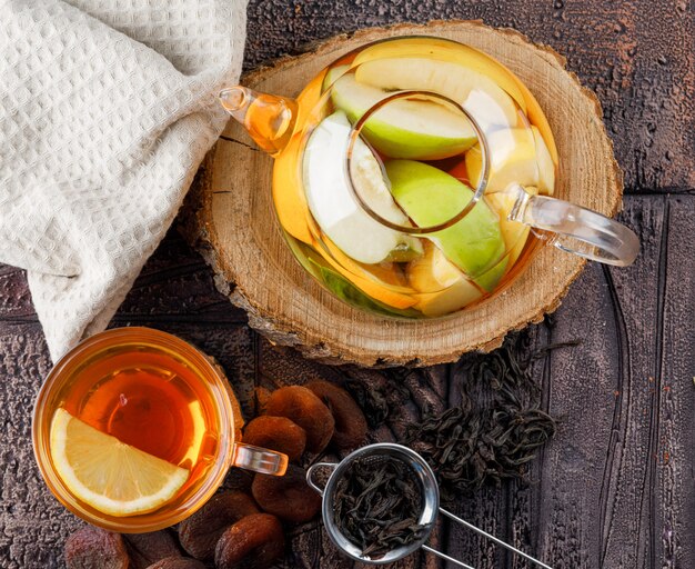 Água com infusão de frutas no bule de chá com damascos secos, madeira, toalha de cozinha, recipiente liso estava deitado sobre uma superfície de telha de pedra