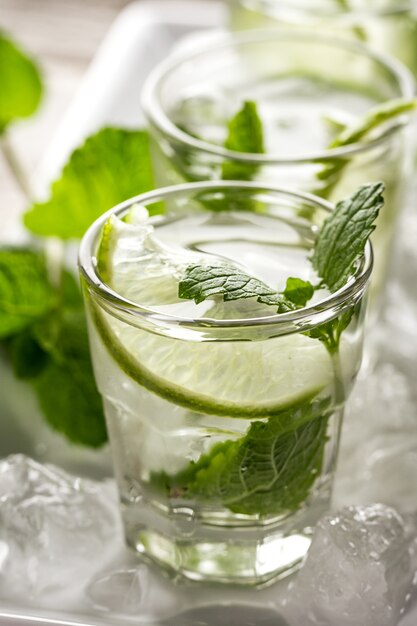 Água de desintoxicação refrescante e gostosa e saudável em óculos com lima, hortelã e gelo em fundo de madeira. Fechar-se. Conceito de Vida Saudável.