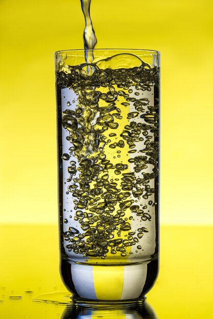 Água derramando em vidro sobre parede amarela