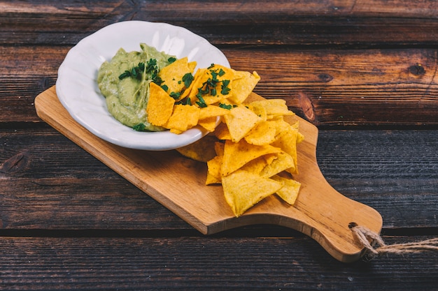 Guacamole em tigela com nachos mexicanos na tábua de madeira