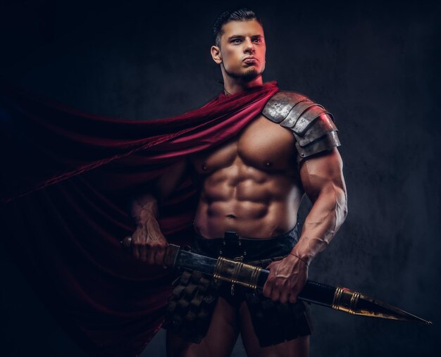 Guerreiro brutal da Grécia antiga com um corpo musculoso em uniformes de batalha posando em um fundo escuro.