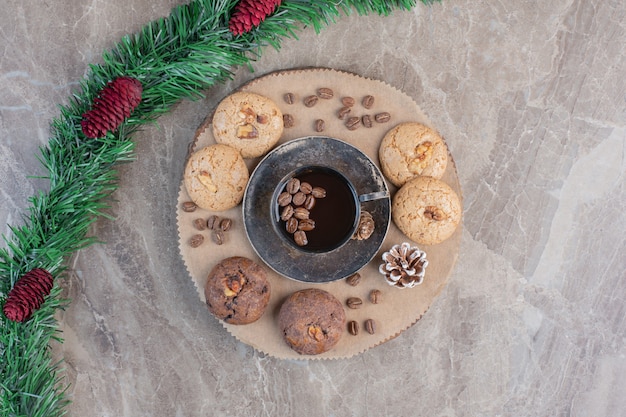 Guirlanda adornada com pinha ao lado de uma travessa de biscoitos e café em mármore.