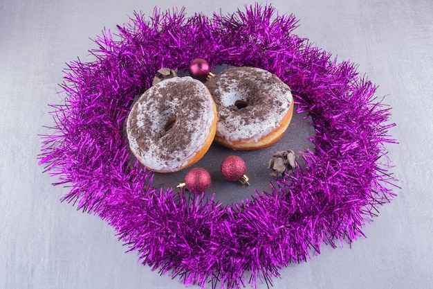 Guirlanda roxa ao redor de donuts vitrificados em uma placa de madeira no fundo branco.